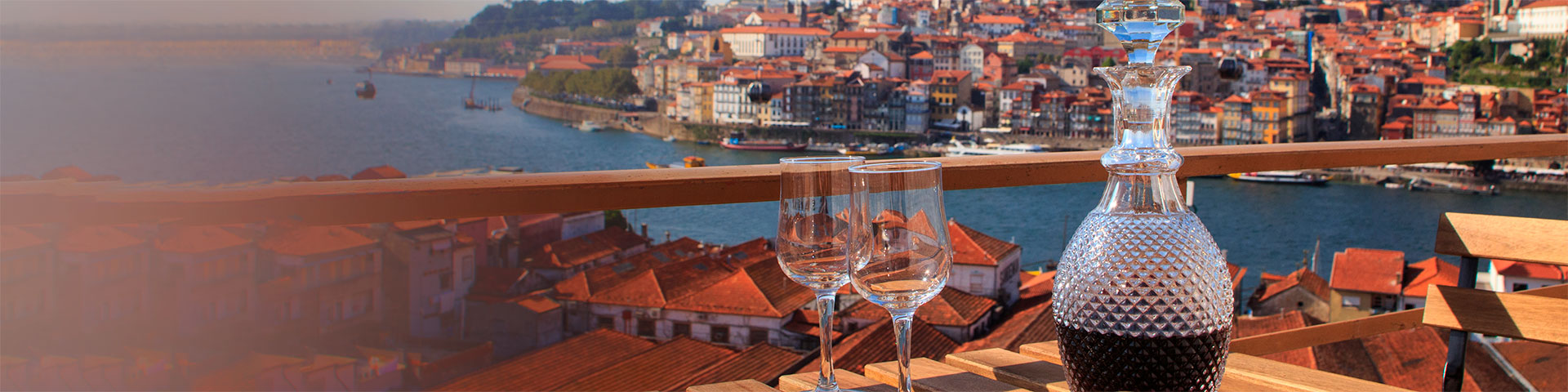 Übersetzungsbüro Portugiesisch: Tisch mit Portwein im Vordergrund und Blick auf den Fluss in Porto, Portugal.
